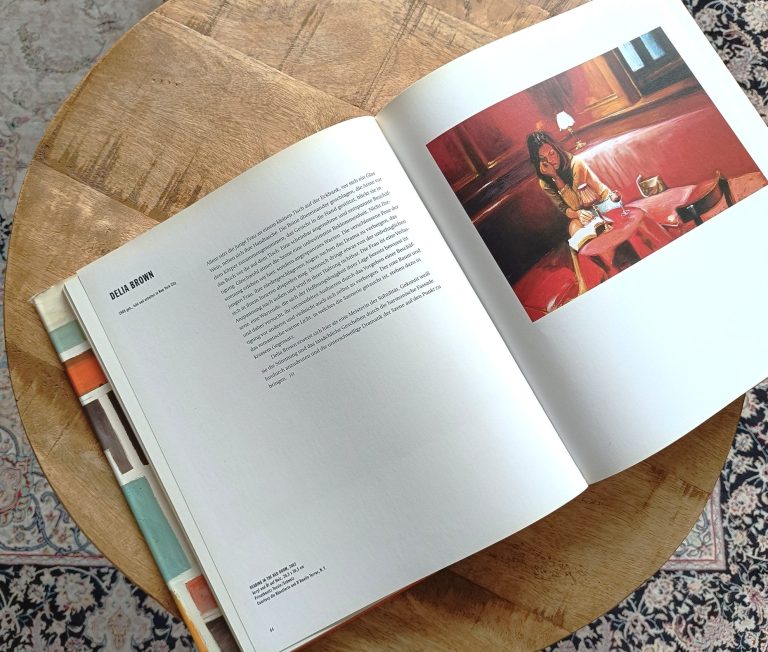 Strasser Design Ingenium – Grafikdesign, Texte, Konzepte Aufgeschlagener Kunstband auf einem kleinen runden Holztisch.