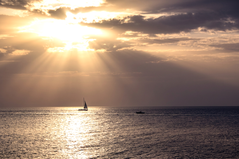 Segelboot auf ruhigem Meer unter strahlendem Sonnenuntergang mit Wolken.