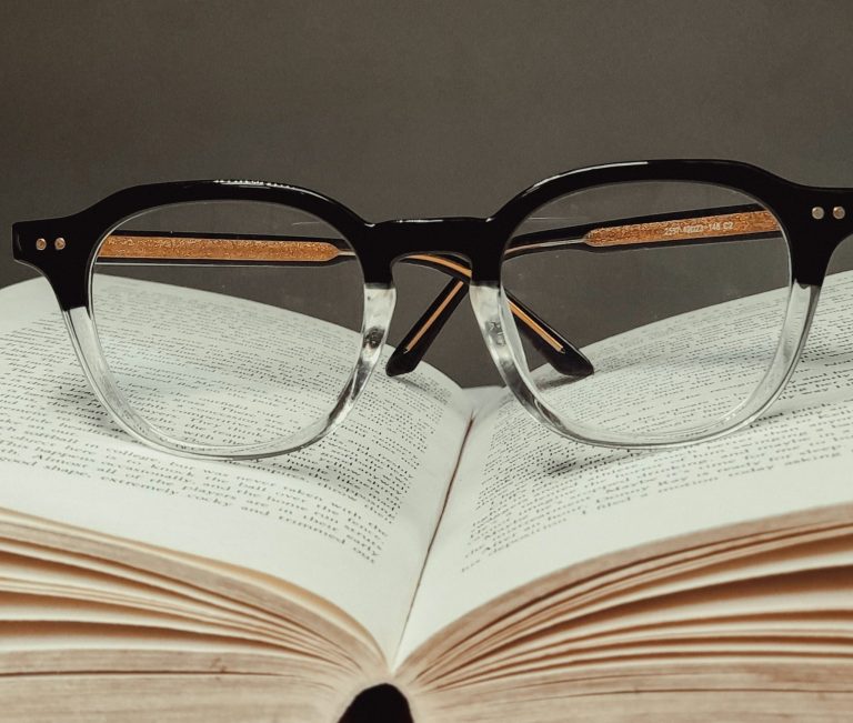 Strasser Design Ingenium – Grafikdesign, Texte, Konzepte Hornbrille liegt auf einem aufgeschlagenen Buch