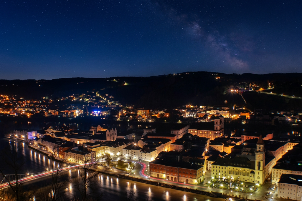 Nachtansicht der Stadt an einem Fluss, beleuchtet von Straßen- und Gebäudelichtern.