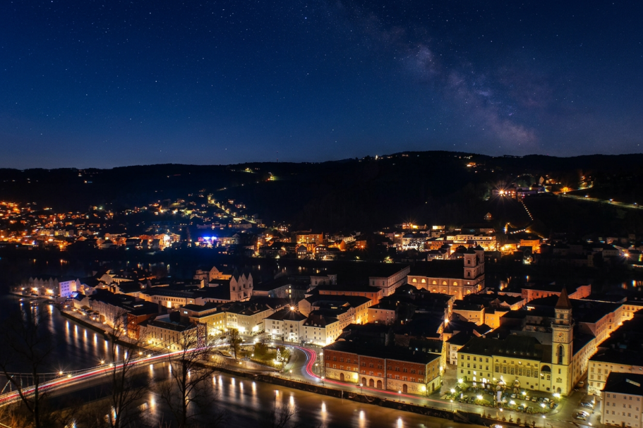Nachtansicht der Stadt an einem Fluss, beleuchtet von Straßen- und Gebäudelichtern.