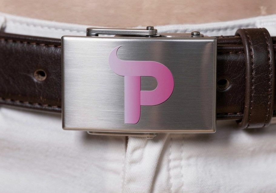 Metallische Gürtelschnalle mit einem pinken „P“ auf einem braunen Gürtel.