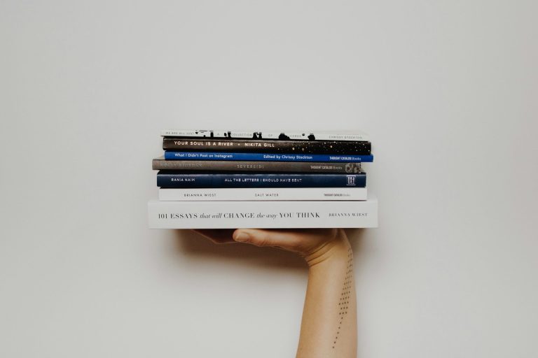 Strasser Design Ingenium – Grafikdesign, Texte, Konzepte Hand hält mehrere Bücher in die Luft.