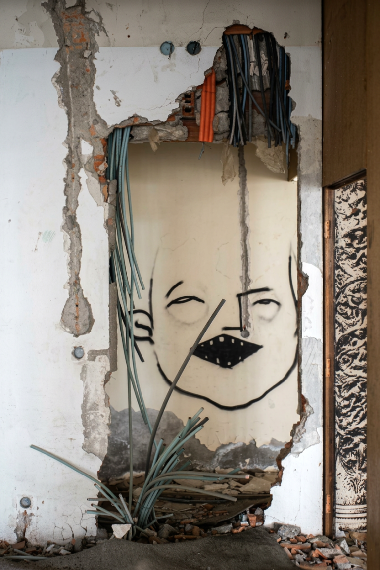 Graffiti eines Gesichts auf einer beschädigten Wand mit freiliegenden Drähten.