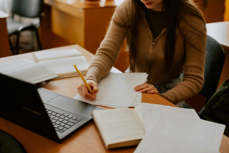 Strasser Design Ingenium – Grafikdesign, Texte, Konzepte Lernende Frau an einem Schreibtisch mit Büchern und Laptop.